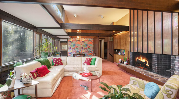 big open living room with cross beams, a fireplace, and a patterned wall