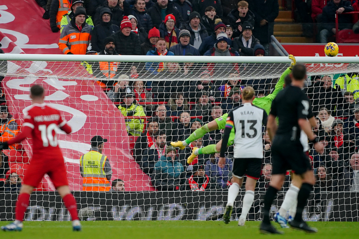 In the background, Fulham keeper Bernd Leno dives toward a shot by Alexis Mac Allister of Liverpool, out of focus in the foreground.