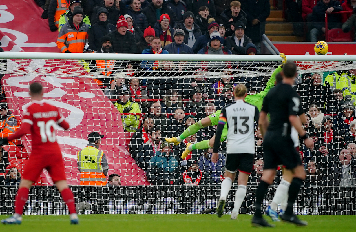 In the background, Fulham keeper Bernd Leno dives toward a shot by Alexis Mac Allister of Liverpool, out of focus in the foreground.