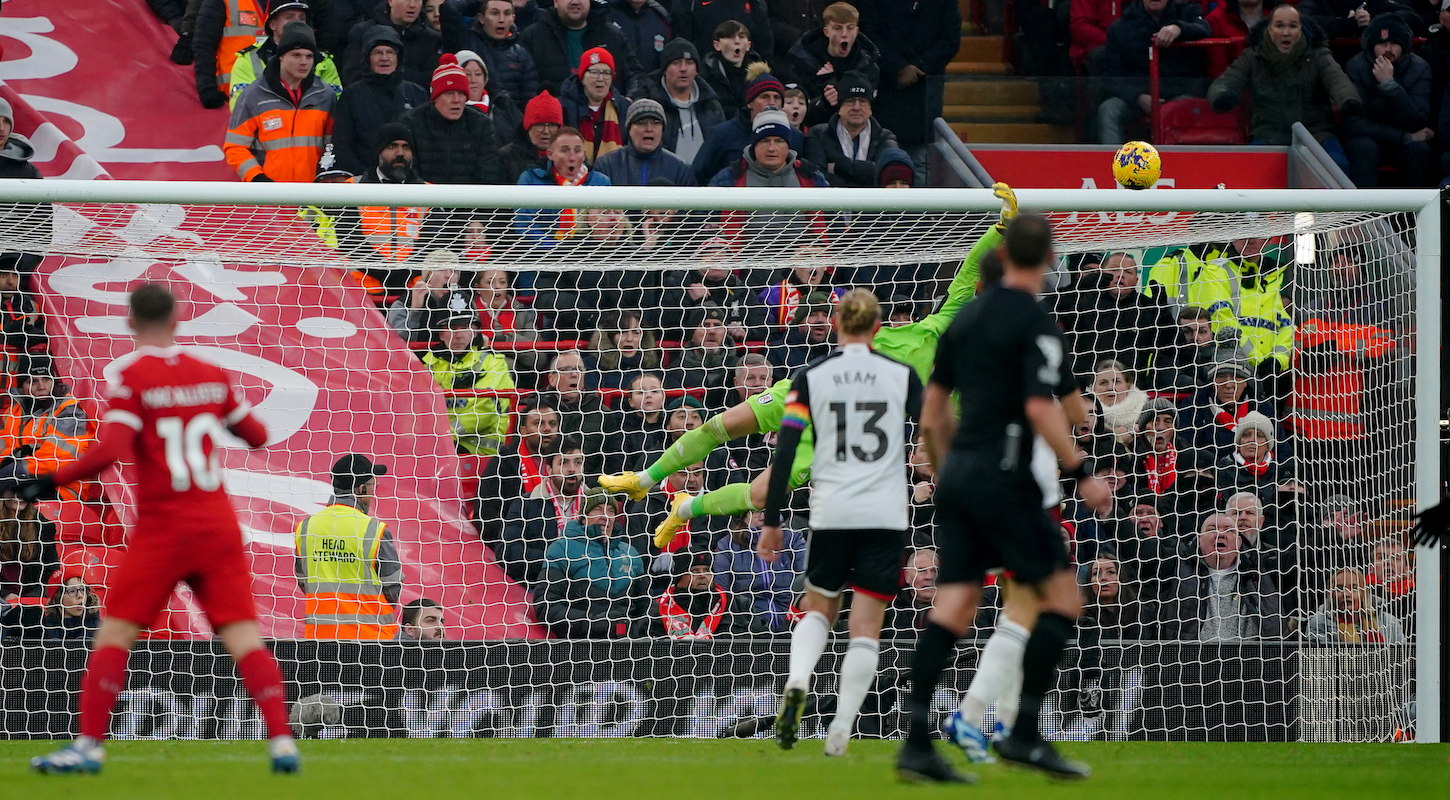 In the background, Fulham keeper Bernd Leno dives toward a shot by Alexis Mac Allister of Liverpool, out of focus in the foreground.