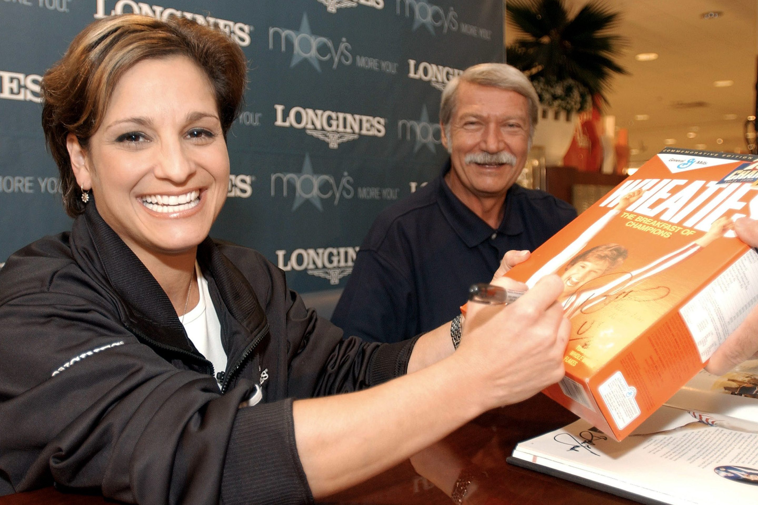 Mary Lou Retton signs a Wheaties box in 2003. By her side is her longtime coach, Bela Karolyi