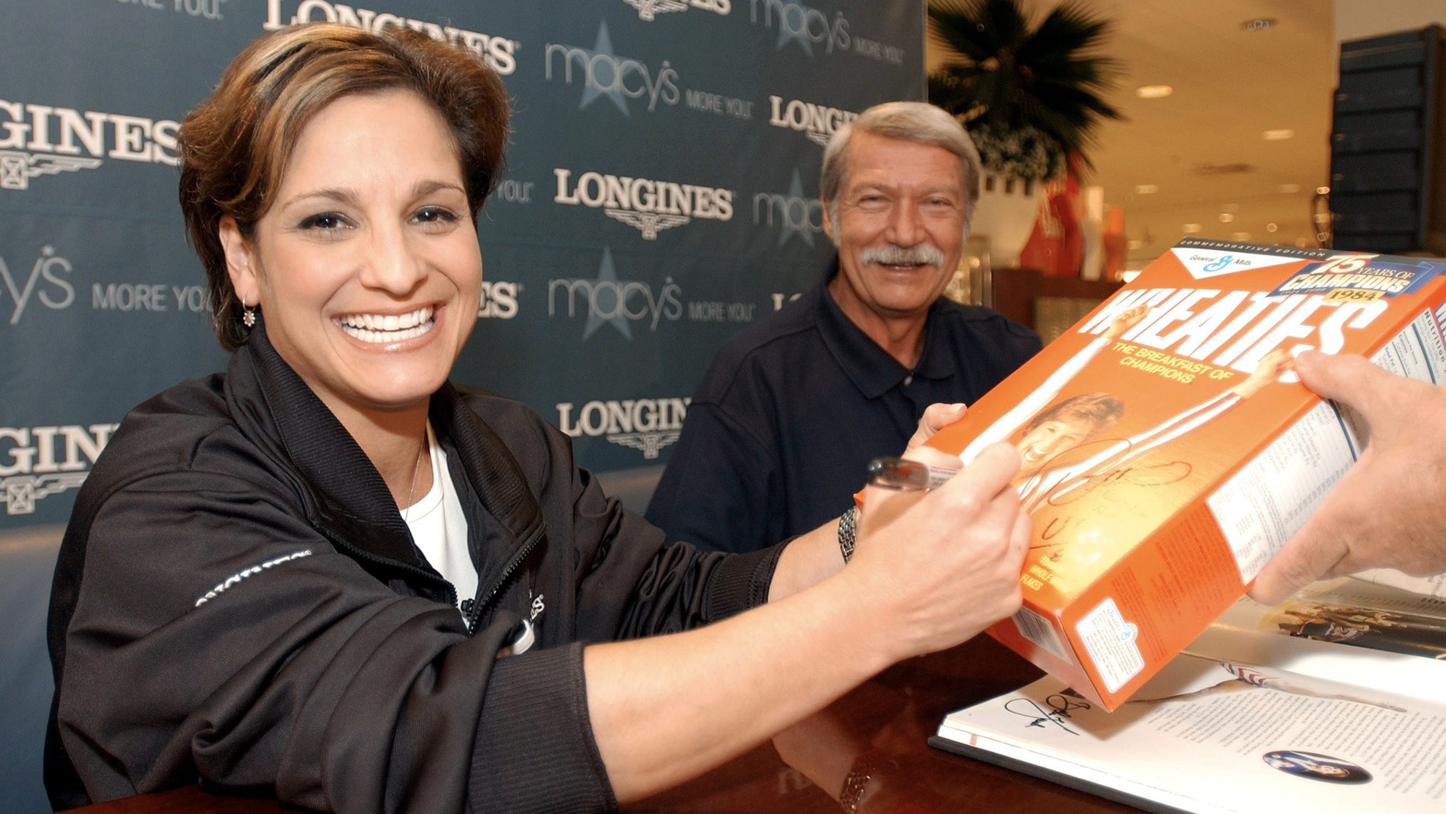 Mary Lou Retton signs a Wheaties box in 2003. By her side is her longtime coach, Bela Karolyi