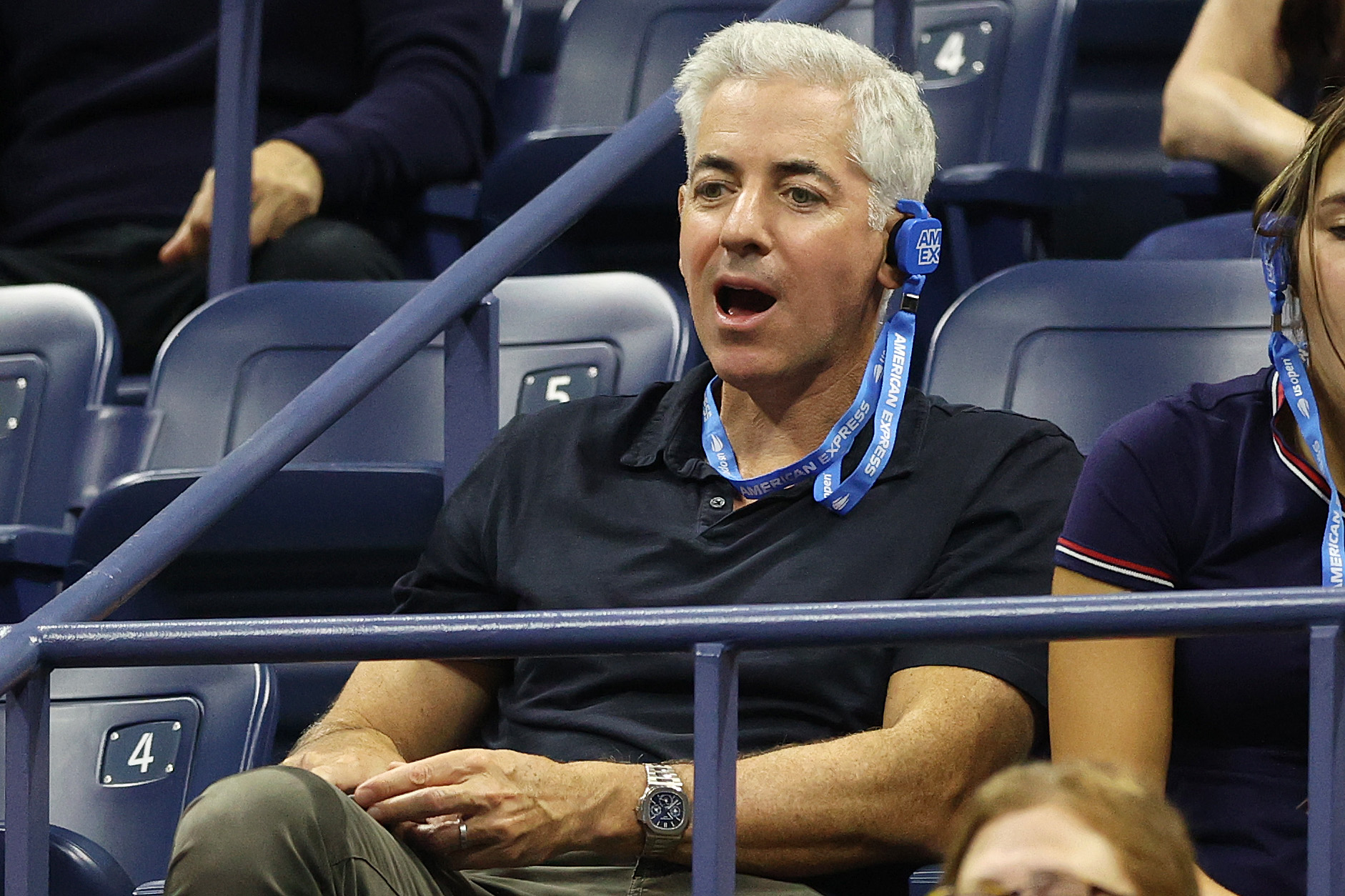 Investor Bill Ackman, wearing one of those goofy headsets you can rent that play the radio broadcast, watches Emma Radacanu play at the 2021 U.S. Open in Queens, NY.