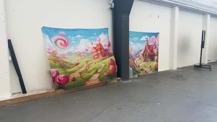 Two posters of a whimsical candy land propped up against the blank walls of a warehouse space