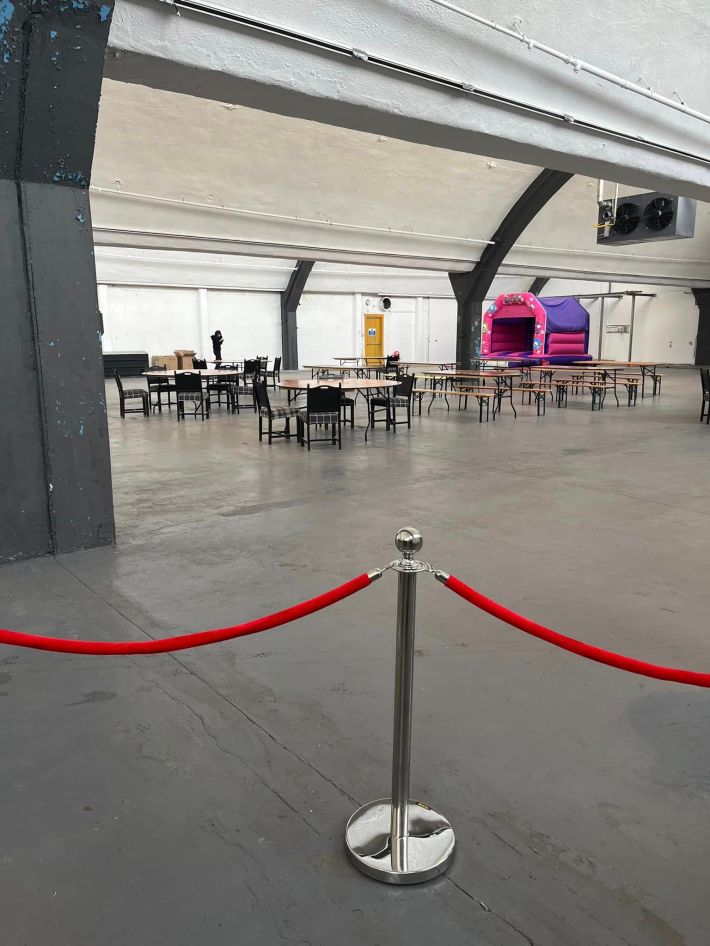 Empty tables and chairs in a warehouse behind a velvet rope