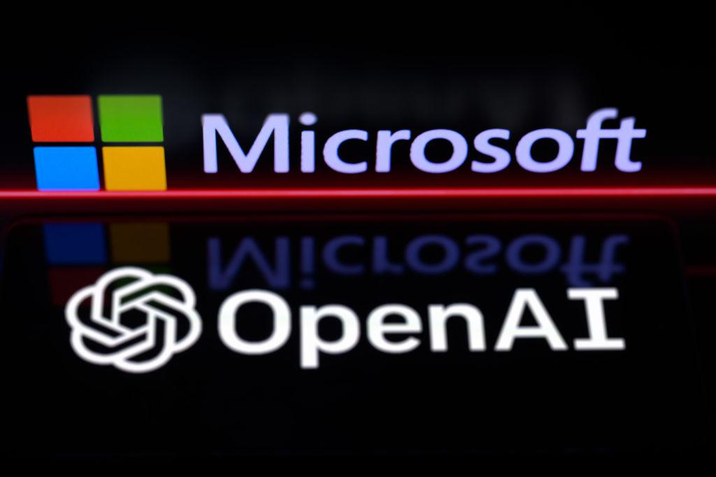 The OpenAI logo is being displayed on a smartphone, with the Microsoft logo visible on the screen in the background.