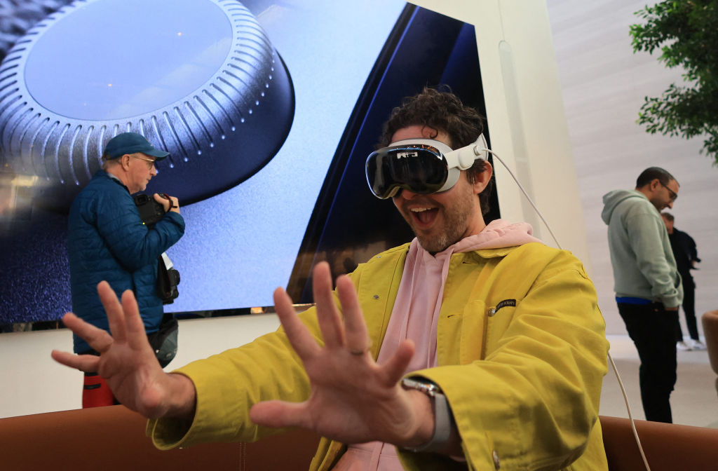 A man sitting in an Apple Store in Los Angeles demos the Apple Vision Pro with his hands held wide apart in a very silly way.