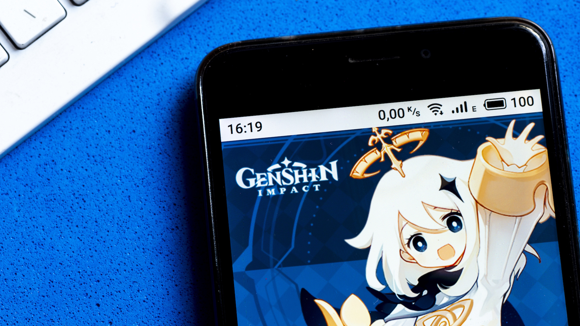 A Genshin Impact app by miHoYo Limited logo is seen displayed on a smartphone.