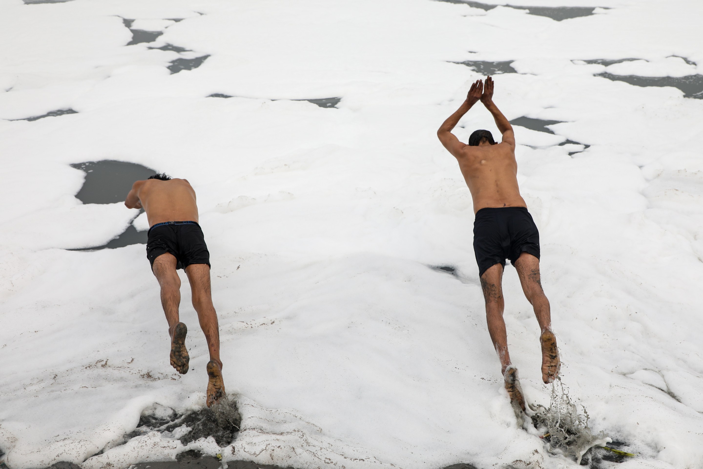 Two divers jump into the foamy Yamuna River