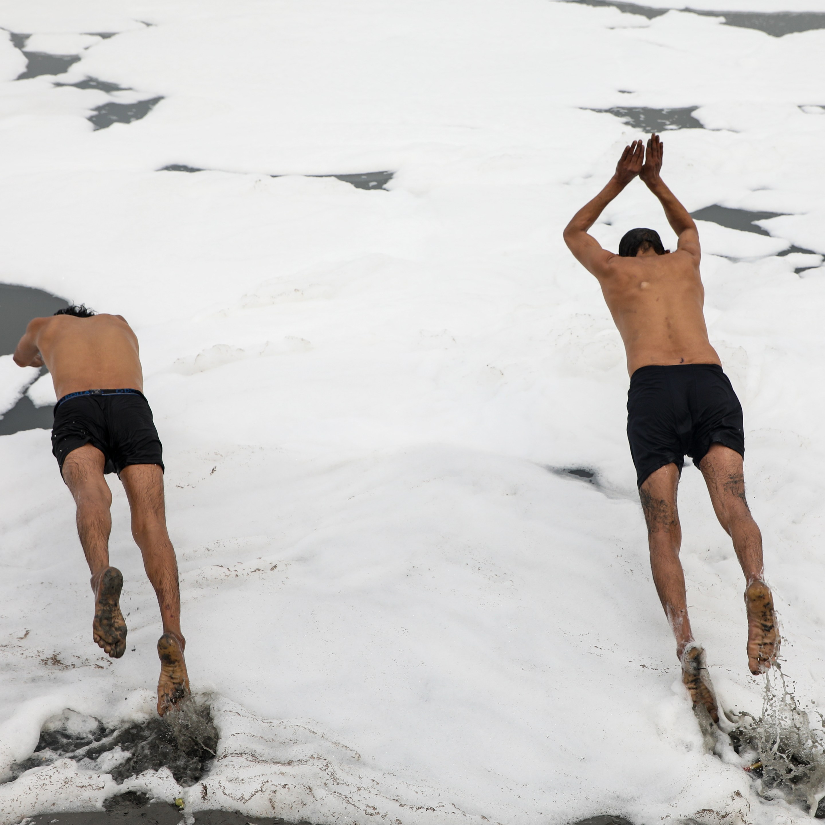 Two divers jump into the foamy Yamuna River