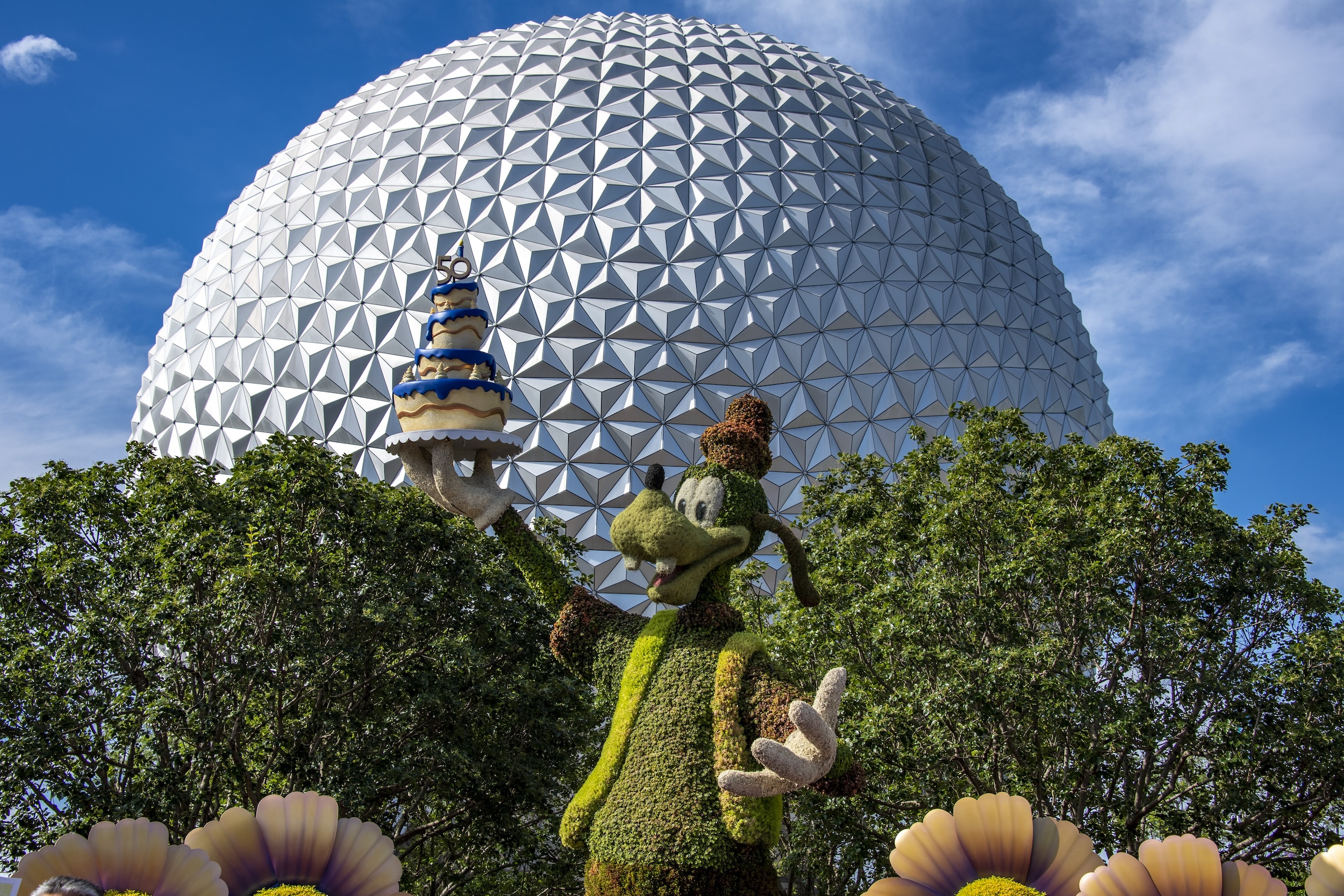 A topiary of Goofy stands with the Spaceship Earth ball in the background.