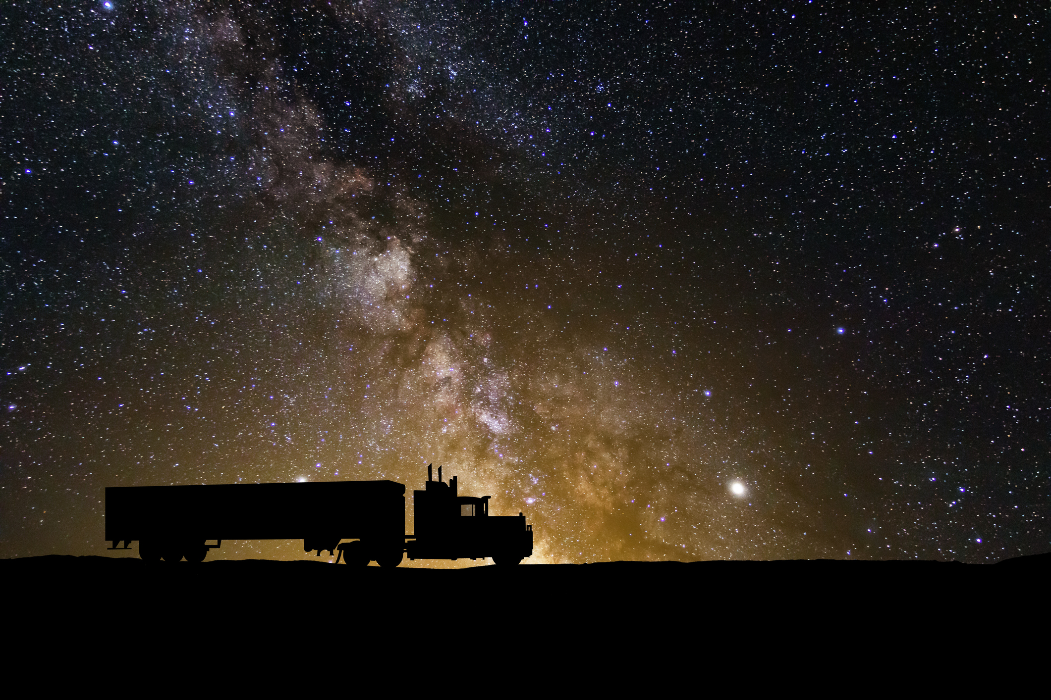 a silhouette of a semi truck in front of a starry sky