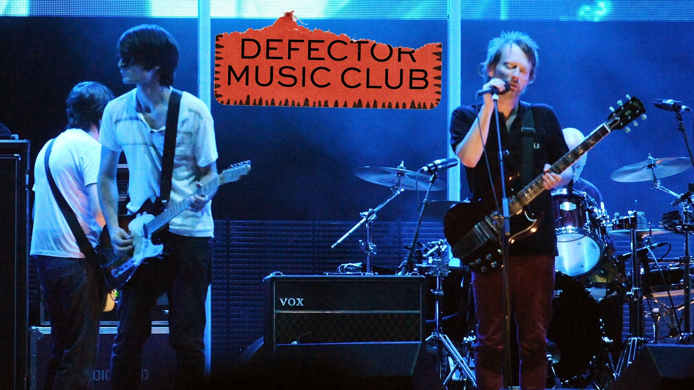 Radiohead performing onstage in support of their 2007 album "In Rainbows," with the Defector Music Club logo right in the middle.