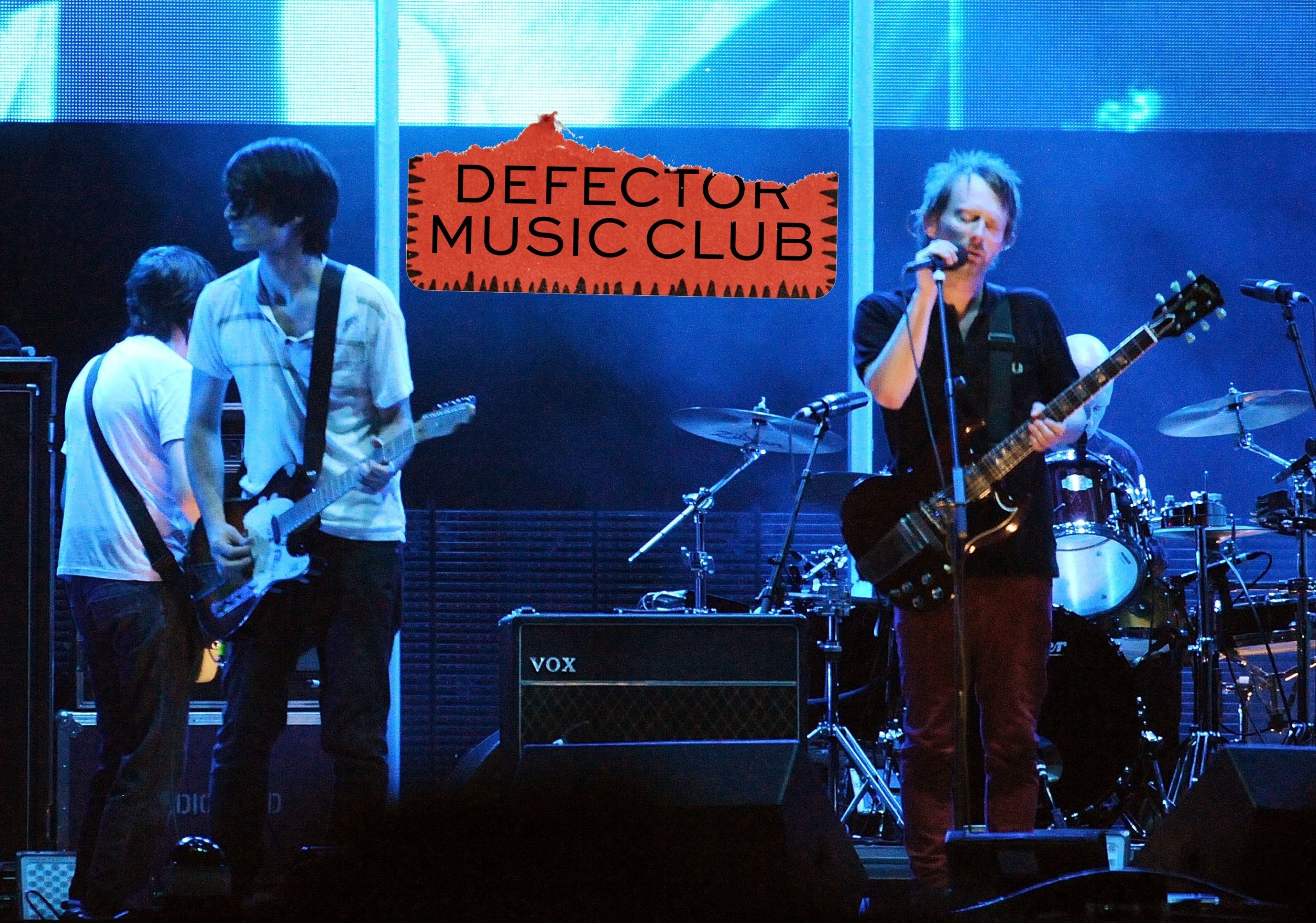 Radiohead performing onstage in support of their 2007 album "In Rainbows," with the Defector Music Club logo right in the middle.