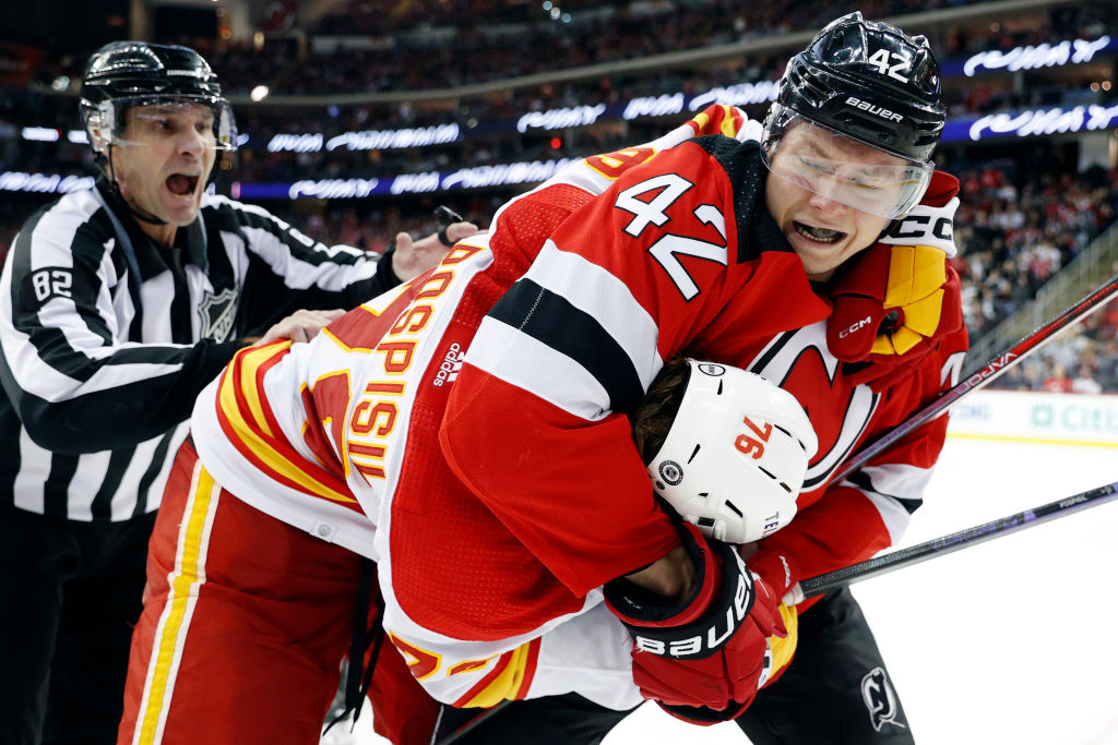 Curtis Lazar #42 of the New Jersey Devils and Martin Pospisil #76 of the Calgary Flames fight while a linesman reacts