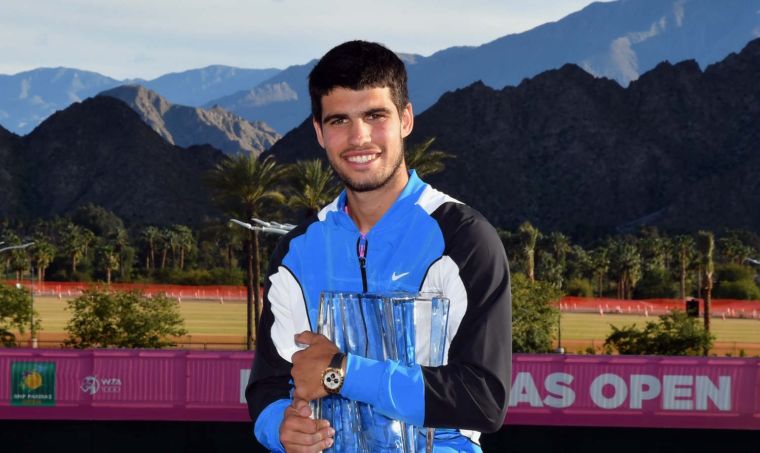 Carlos Alcaraz smiles with Indian Wells trophy in front of mountains