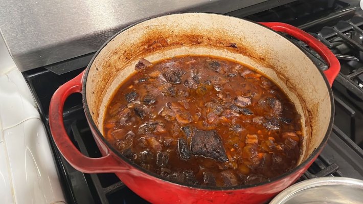 The same dutch oven from earlier, but now its contents are cooked; their colors have darkened and there's a slick of rendered fat across the surface of the liquid.