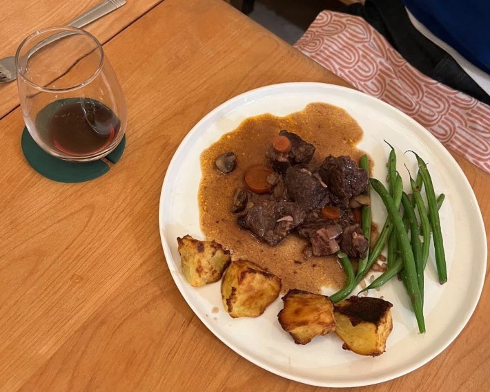 A plate of beef bourguignon with roasted potatoes and green beans.