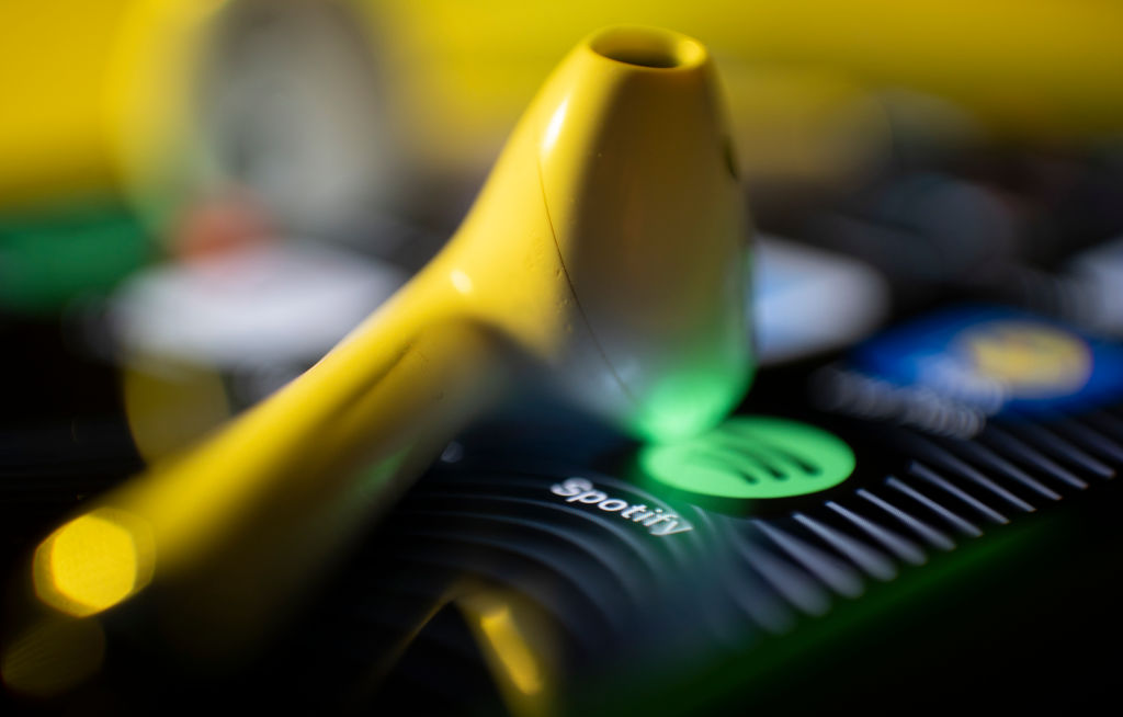 A photo showing an ear bud resting on the screen of a smartphone showing the Spotify music app.
