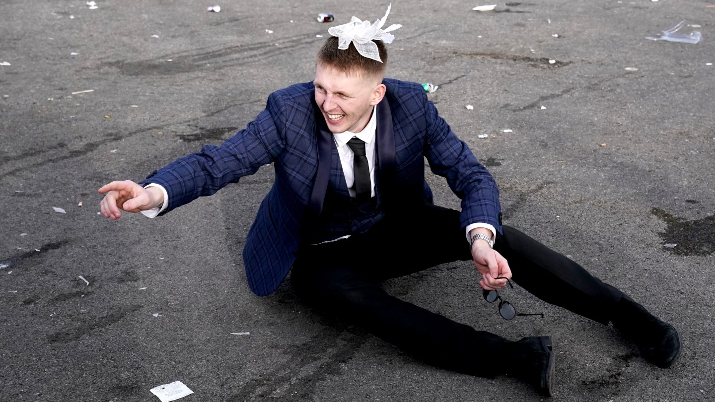 A racegoer sits on the floor, bowtie atop his head, at the end of day two of the 2024 Randox Grand National Festival at Aintree Racecourse, Liverpool.