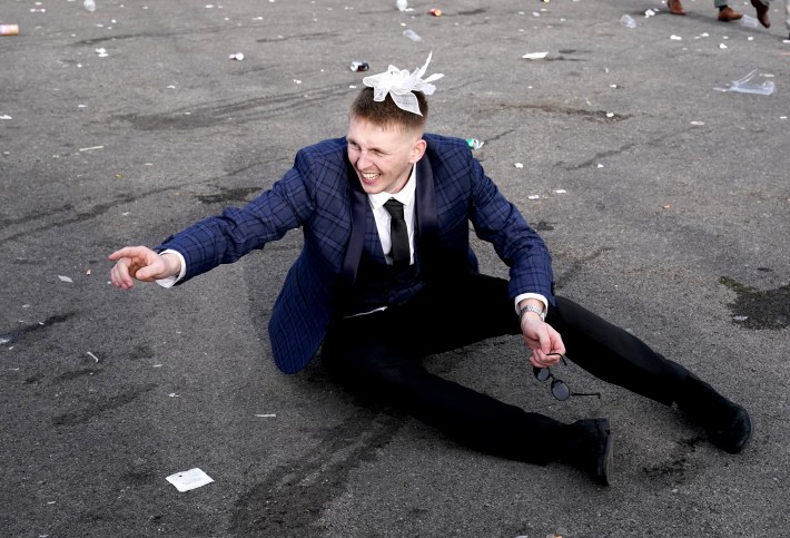 A racegoer sits on the floor, bowtie atop his head, at the end of day two of the 2024 Randox Grand National Festival at Aintree Racecourse, Liverpool.