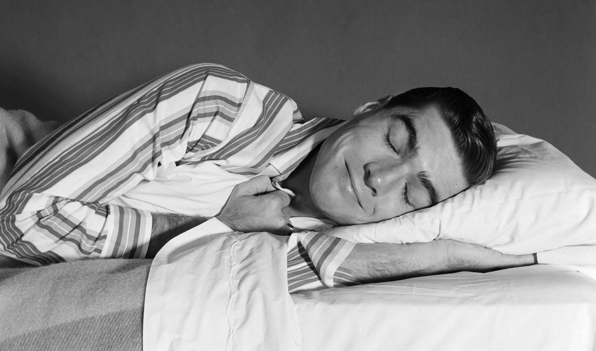 1950s 1960s MAN IN STRIPED PAJAMAS SMILING ASLEEP IN BED (Photo by ClassicStock/Getty Images)