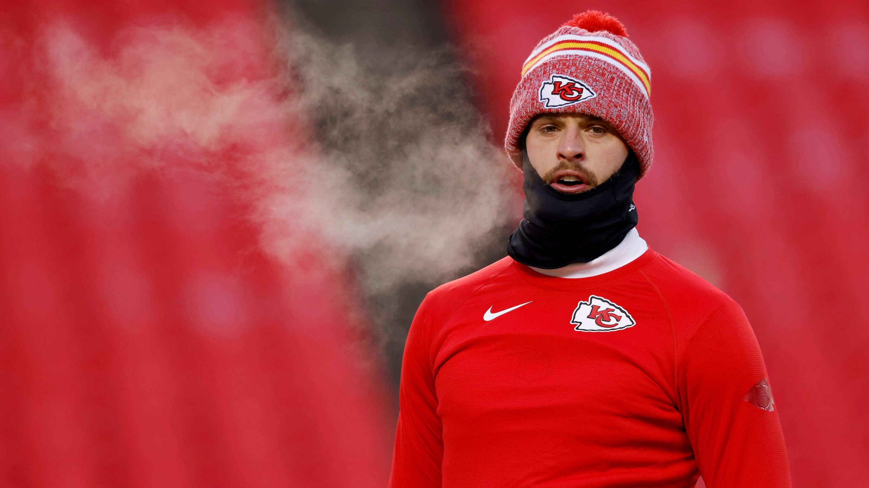 Harrison Butker wearing a knit cap and a cowl while warming up on the field in cold temperatures before the Chiefs' January 13, 2024 Wild Card game.