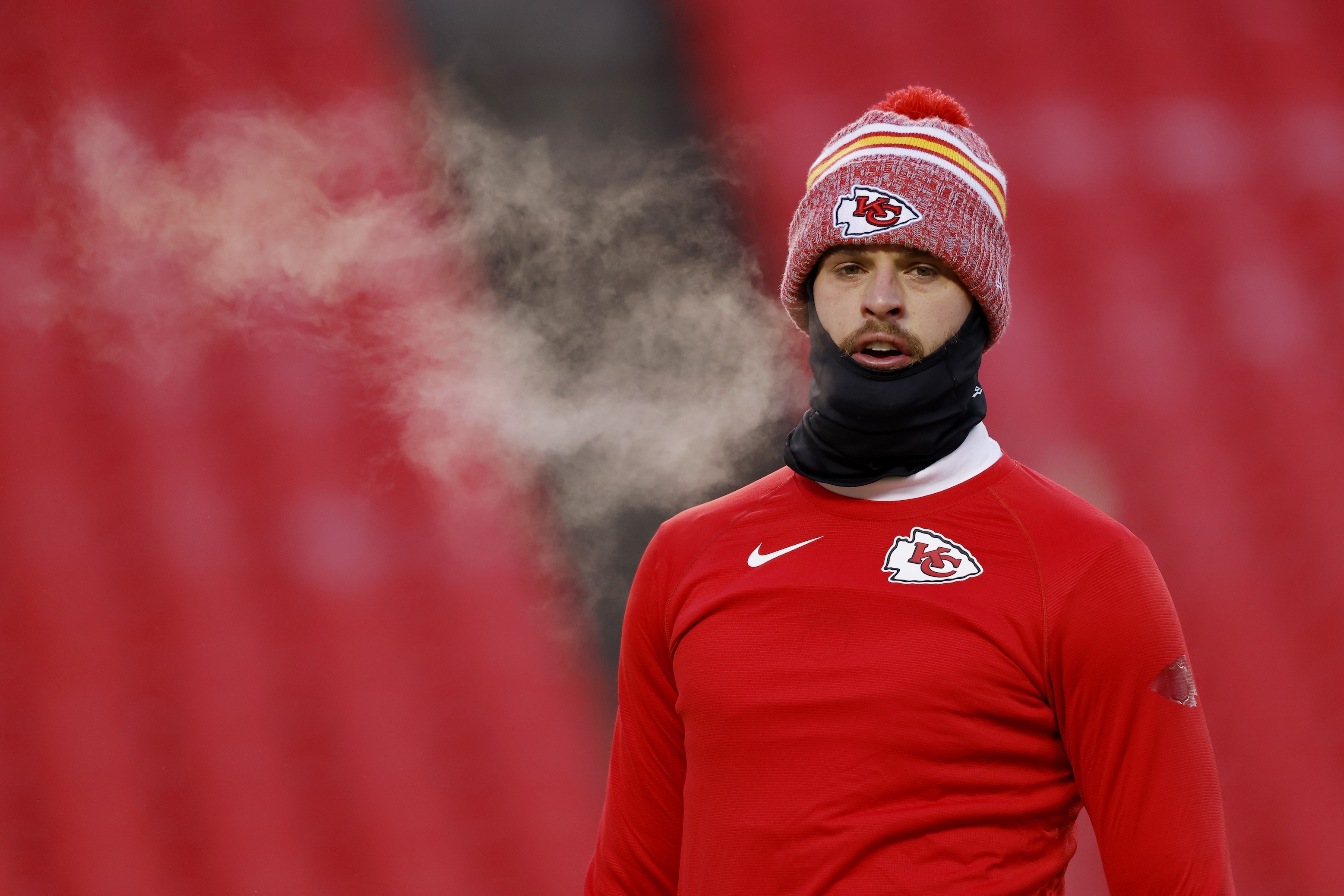Harrison Butker wearing a knit cap and a cowl while warming up on the field in cold temperatures before the Chiefs' January 13, 2024 Wild Card game.