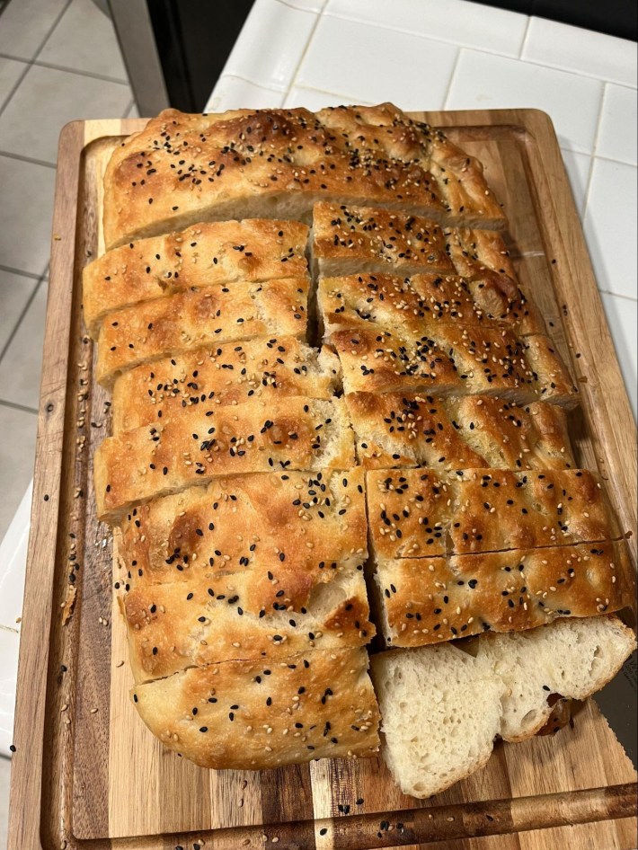 A lovely focaccia loaf, sliced, with black and white sesame seeds on top.
