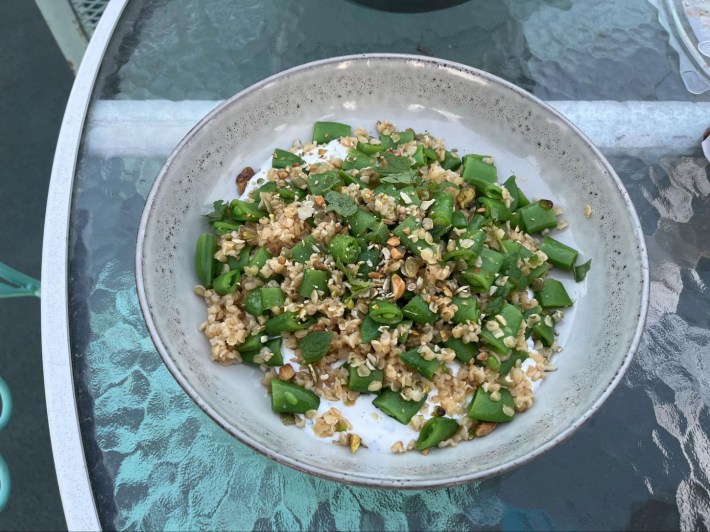 Snap pea and bulgur wheat salad with labneh and dukkah, in a bowl, on a glass tabletop.