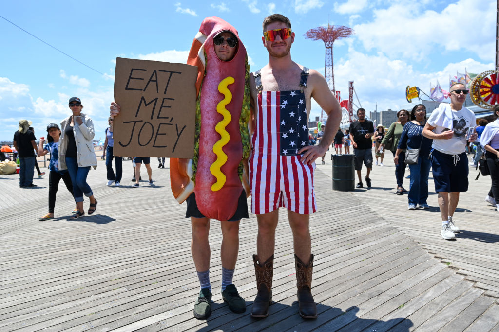 Two men celebrate the July Fourth holiday on the Coney Island boardwalk in New York, one wearing a hot dog costume and the other in red, white and blue overalls.
