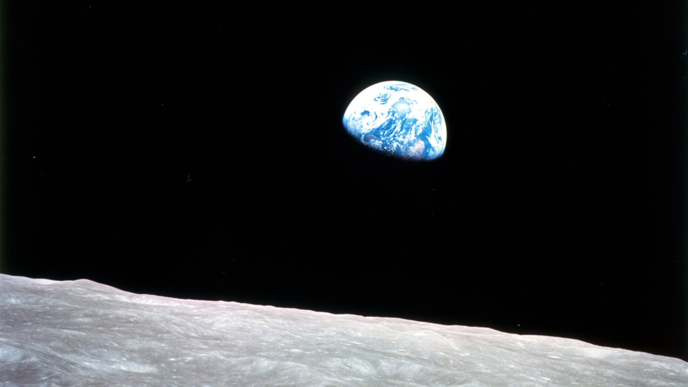 Earthrise - Apollo 8, December 24, 1968. This view of the rising Earth greeted the Apollo 8 astronauts as they came from behind the Moon after the fourth nearside orbit. The photo, by astronaut William Anders, is displayed here in its original orientation, though it is more commonly viewed with the lunar surface at the bottom of the photo. Earth is about five degrees left of the horizon in the photo. The unnamed surface features on the left are near the eastern limb of the Moon as viewed from Earth. The lunar horizon is approximately 780 kilometers from the spacecraft. Height of the photographed area at the lunar horizon is about 175 kilometers.