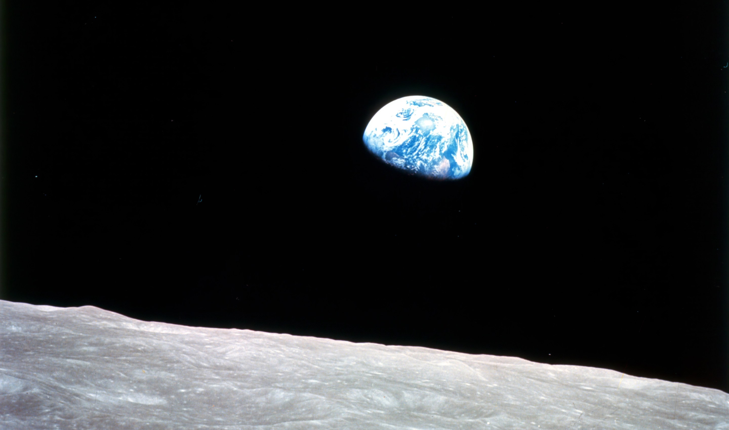 Earthrise - Apollo 8, December 24, 1968. This view of the rising Earth greeted the Apollo 8 astronauts as they came from behind the Moon after the fourth nearside orbit. The photo, by&#xa0;astronaut&#xa0;William Anders, is displayed here in its original orientation, though it is more commonly viewed with the lunar surface at the bottom of the photo. Earth is about five degrees left of the horizon in the photo. The unnamed surface features on the left are near the eastern limb of the Moon as viewed from Earth. The lunar horizon is approximately 780 kilometers from the spacecraft. Height of the photographed area at the lunar horizon is about 175 kilometers.