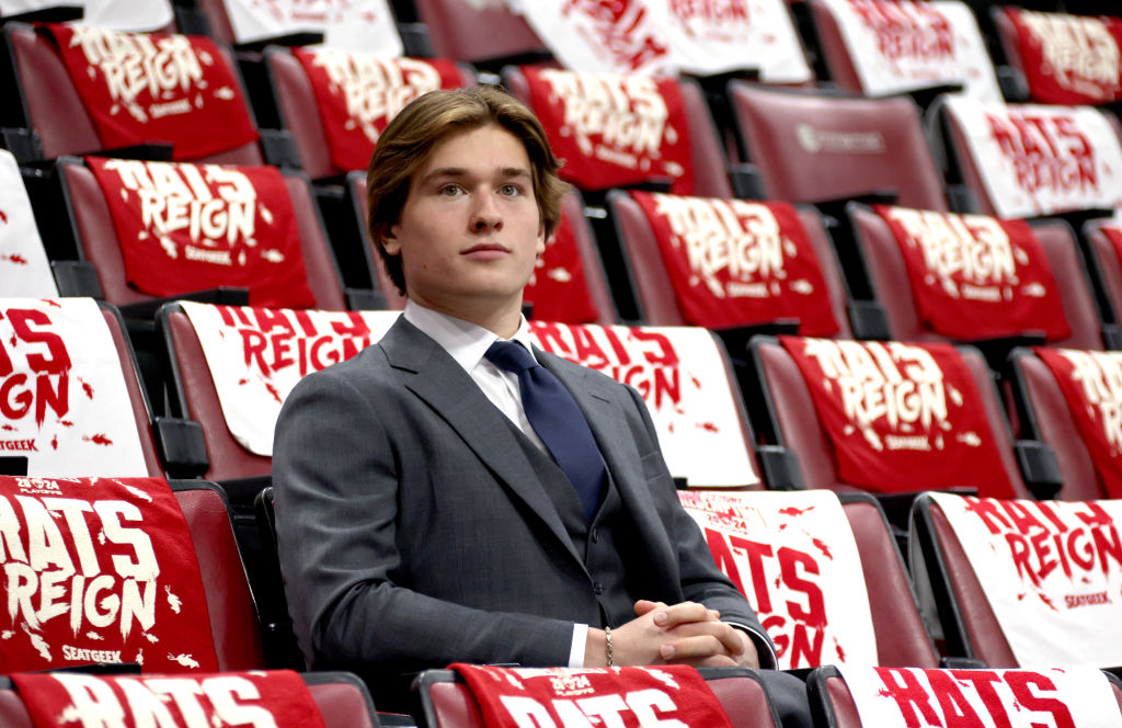 Macklin Celebrini sits in the stands while wearing a suit