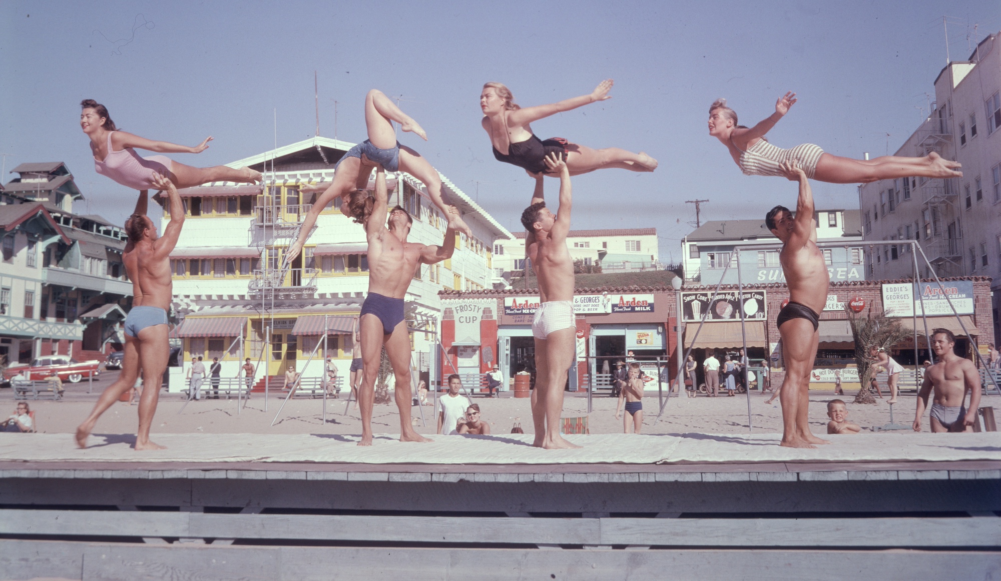 1956: EXCLUSIVE Full-length image of stunt performers on Muscle Beach, Santa Monica, California. Four men lift four women in the air, all in bathing suits, on the boardwalk stage. (Photo by Gene Lester/Getty Images)