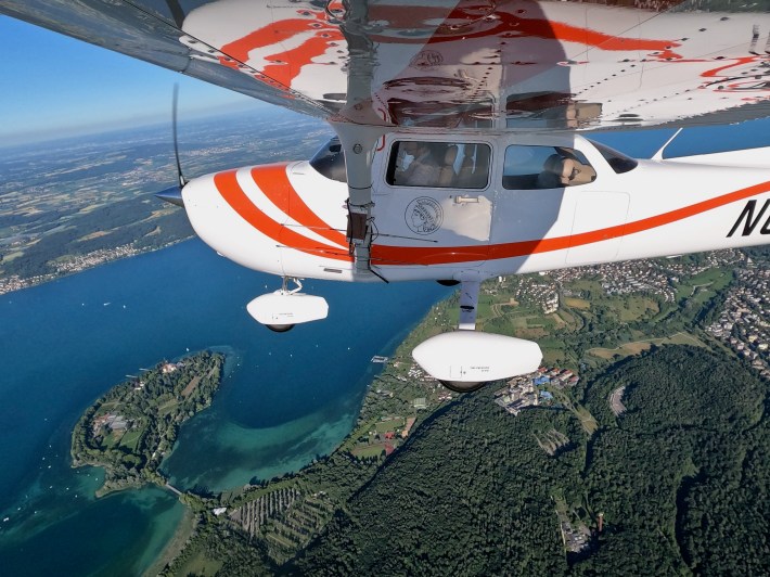 A tiny white and red plane in the sky over an island