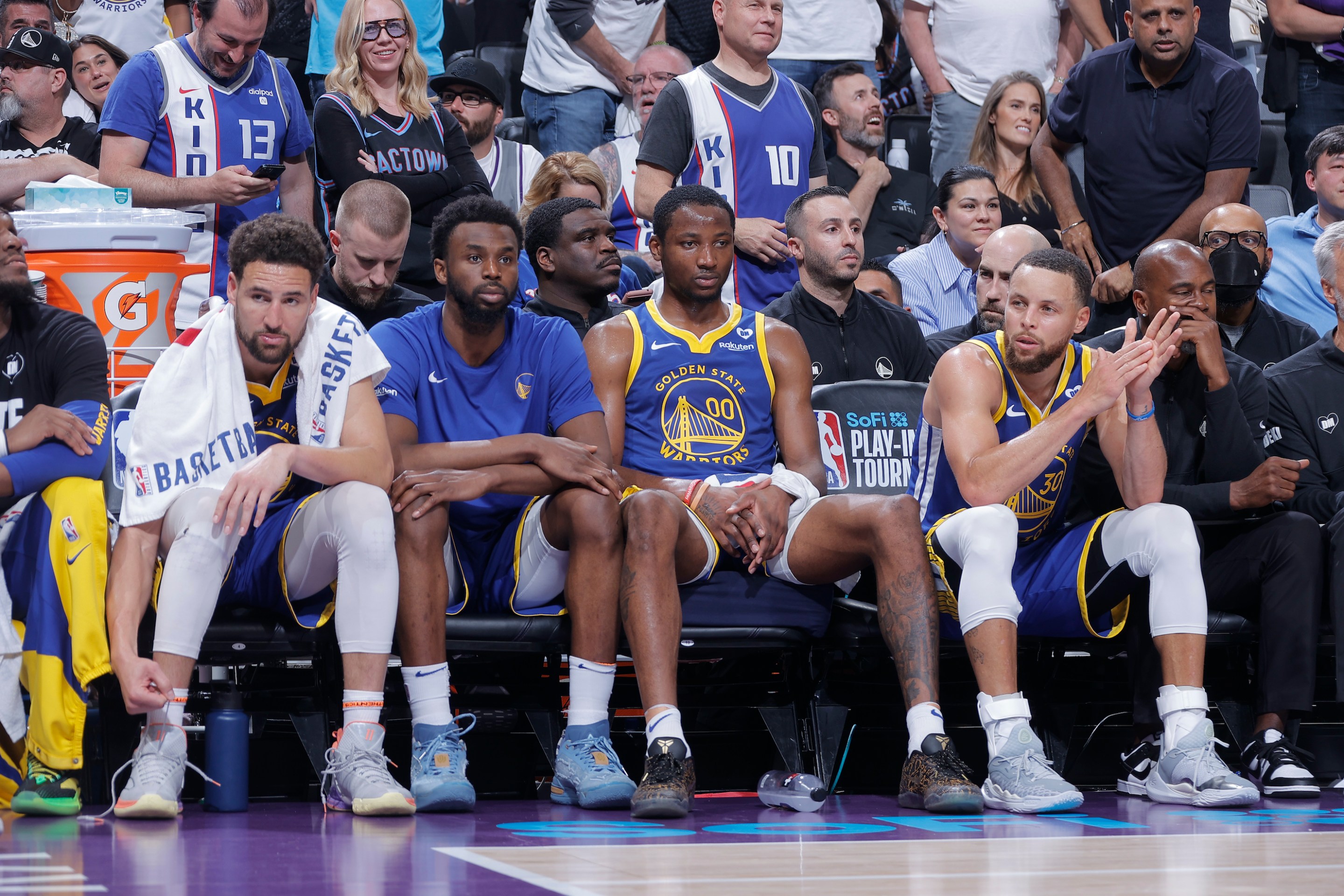 Klay Thompson #11, Andrew Wiggins #22, Jonathan Kuminga #00, and Stephen Curry #30 of the Golden State Warriors look on from the bench during the game against the Sacramento Kings during the 2024 Play-In Tournament