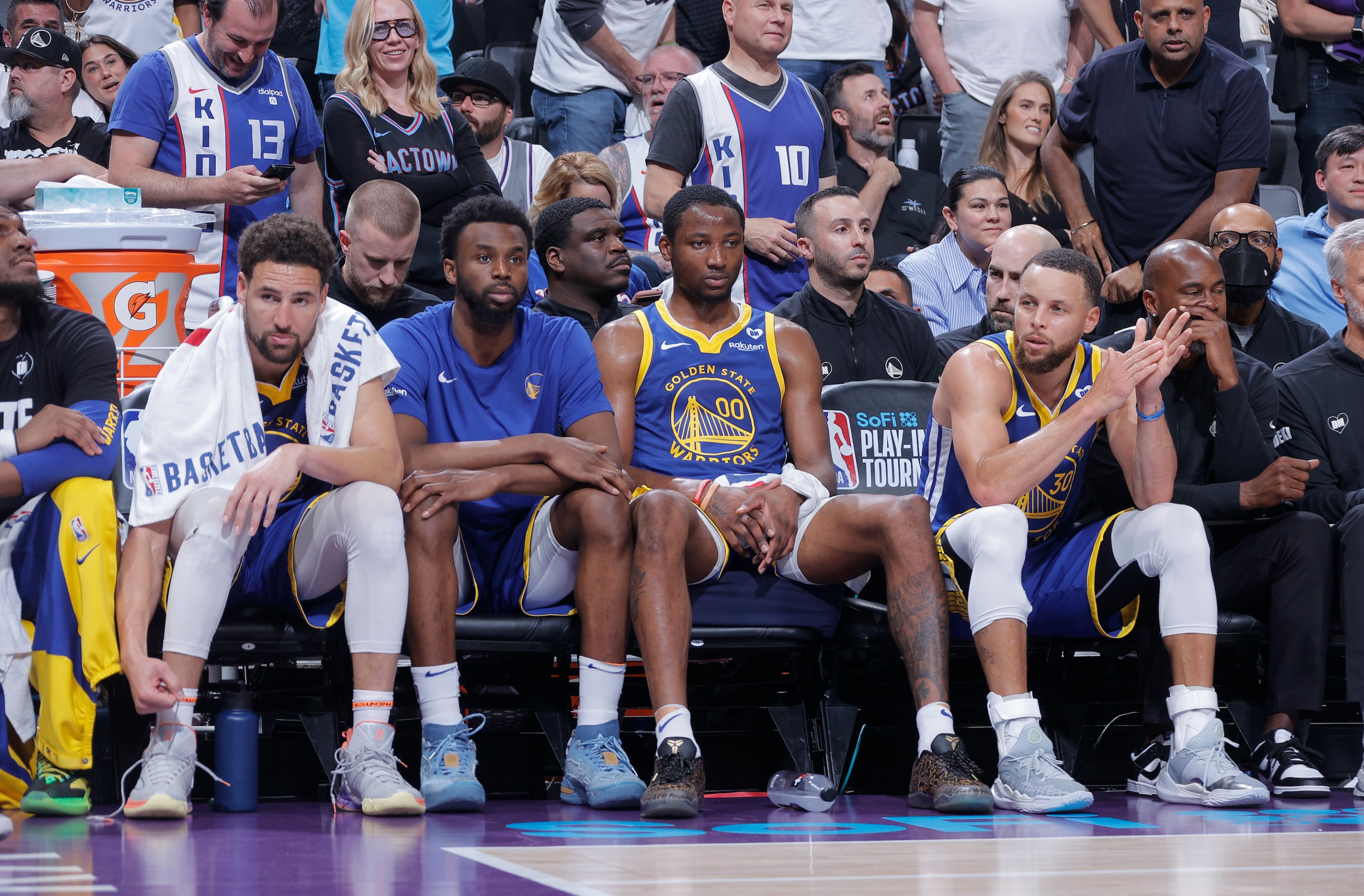 Klay Thompson #11, Andrew Wiggins #22, Jonathan Kuminga #00, and Stephen Curry #30 of the Golden State Warriors look on from the bench during the game against the Sacramento Kings during the 2024 Play-In Tournament