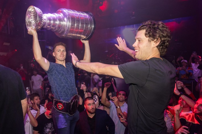 Matthew Tkachuk hoists the cup over his head as Carter Verhaeghe holds out his arms in front of him.