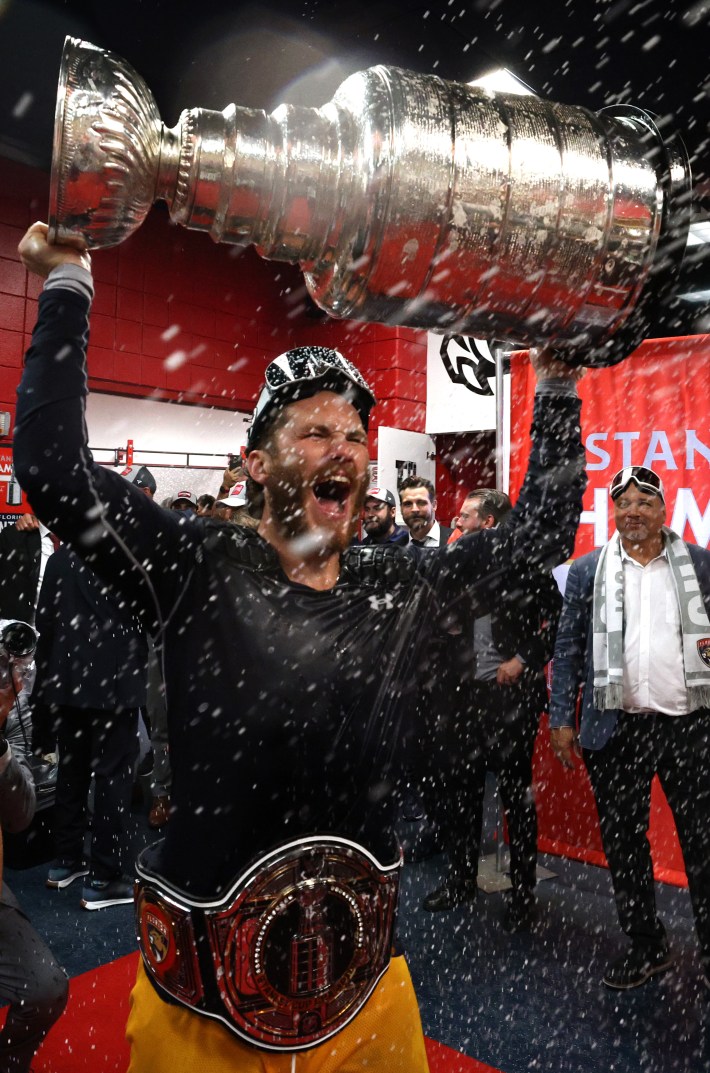 SUNRISE, FLORIDA - JUNE 24: Matthew Tkachuk #19 of the Florida Panthers celebrates with the Stanley Cup while wearing the NHL/WWE Stanley Cup Championship belt in the locker room after Game Seven of the 2024 Stanley Cup Final between the Edmonton Oilers and the Florida Panthers at Amerant Bank Arena on June 24, 2024 in Sunrise, Florida.