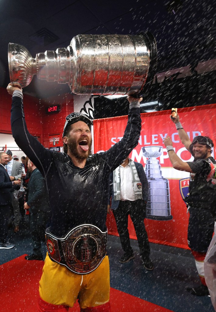 SUNRISE, FLORIDA - JUNE 24: Matthew Tkachuk #19 of the Florida Panthers celebrates with the Stanley Cup while wearing the NHL/WWE Stanley Cup Championship belt in the locker room after Game Seven of the 2024 Stanley Cup Final between the Edmonton Oilers and the Florida Panthers at Amerant Bank Arena on June 24, 2024 in Sunrise, Florida.