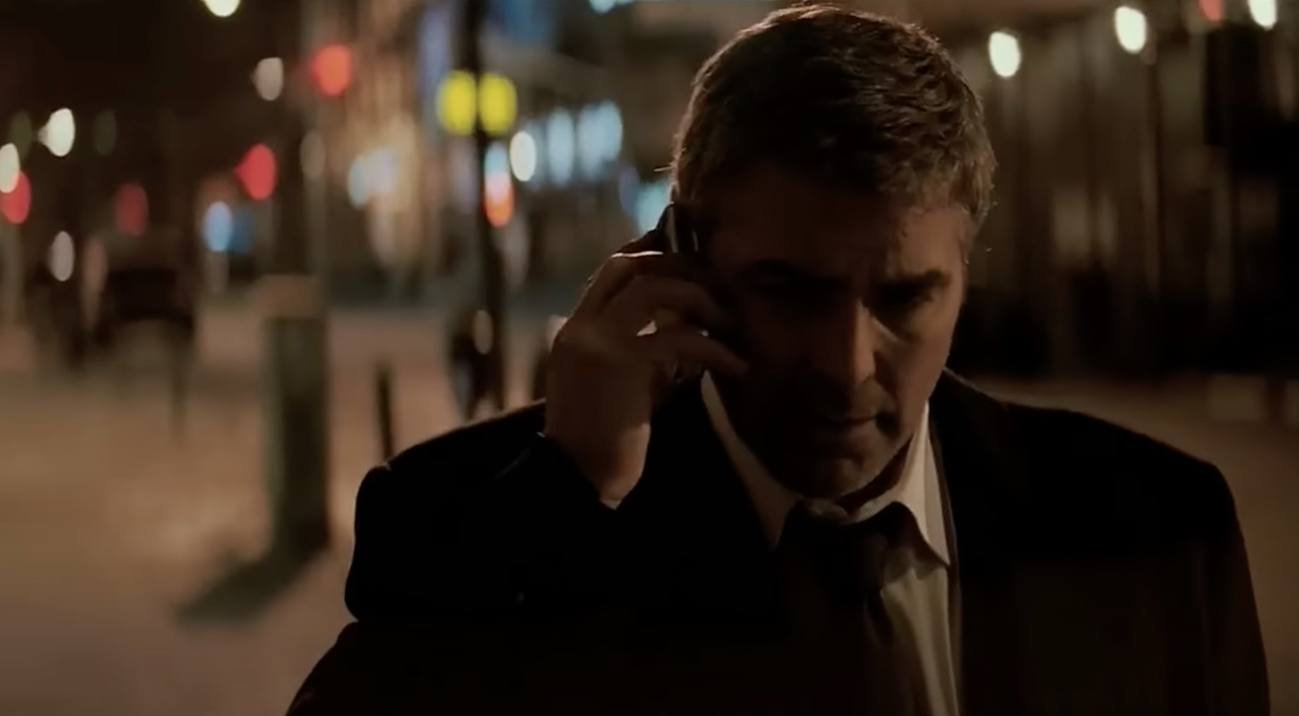 George Clooney, as Michael Clayton, talks into a cell phone while walking down a city street at night.