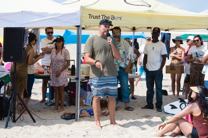 Tyler Breuer speaks in front of two tents to an audience at the Beach Day for Palestine event in Rockaway at Beach 65 St.