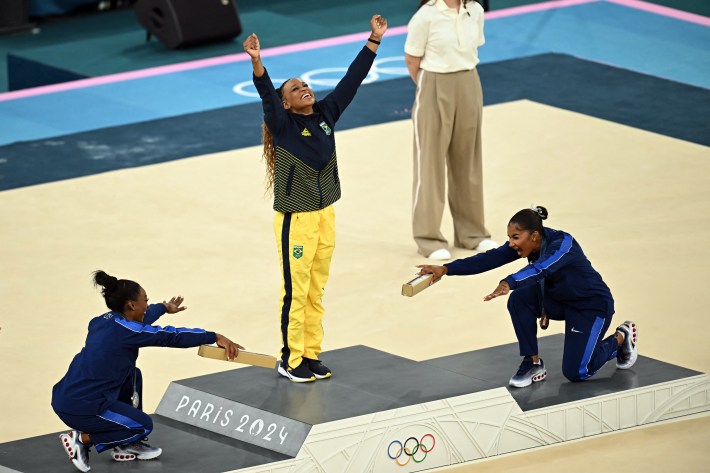 (LtoR) US' Simone Biles (silver), Brazil's Rebeca Andrade (gold) and US' Jordan Chiles (bronze) pose during the podium ceremony for the artistic gymnastics women's floor exercise event of the Paris 2024 Olympic Games at the Bercy Arena in Paris, on August 5, 2024. Biles and Chiles are bowing, while Andrade has her hands in the air, victorious.