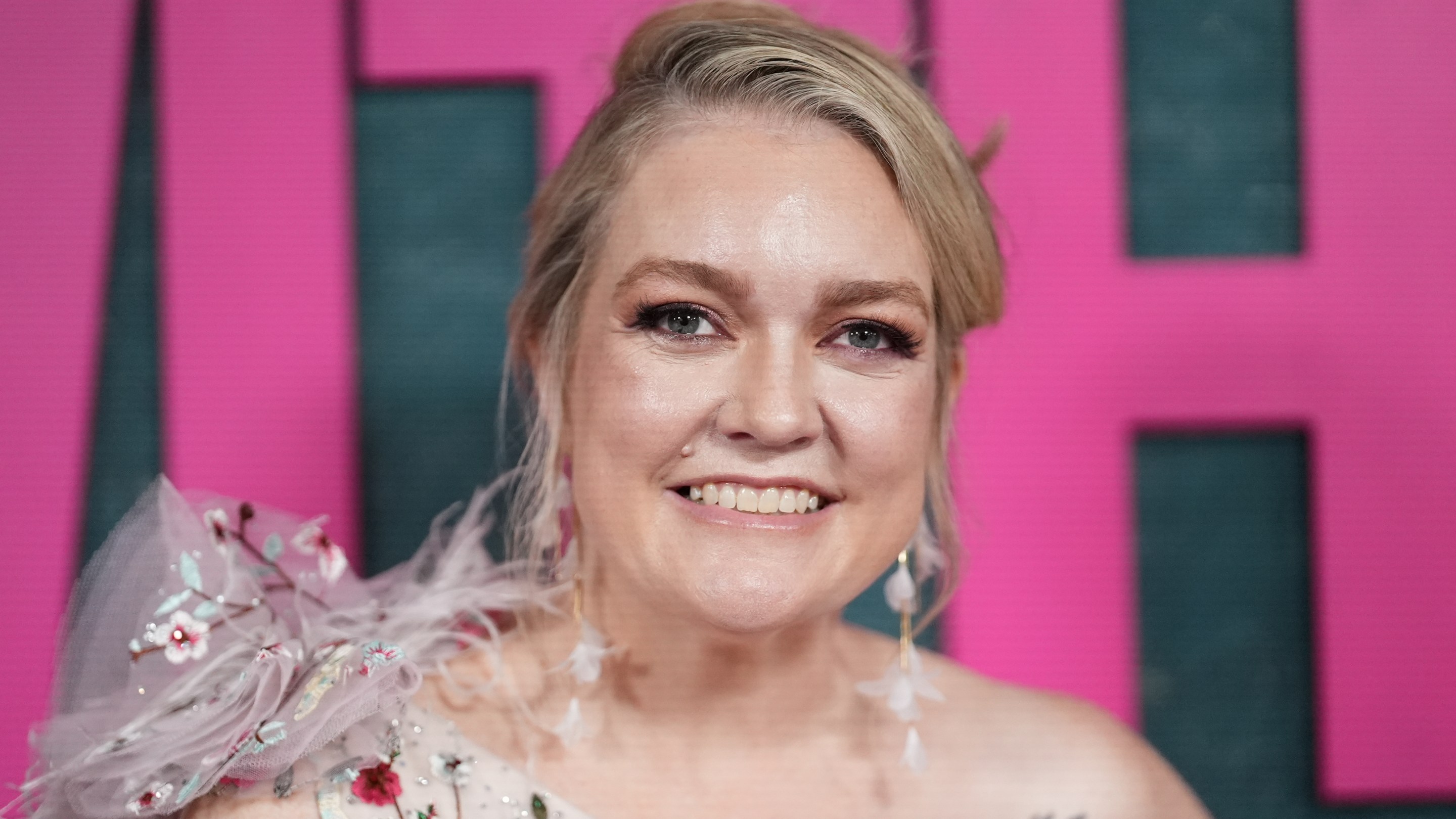 Colleen Hoover, wearing a one-shoulder dress, smiles at the camera.