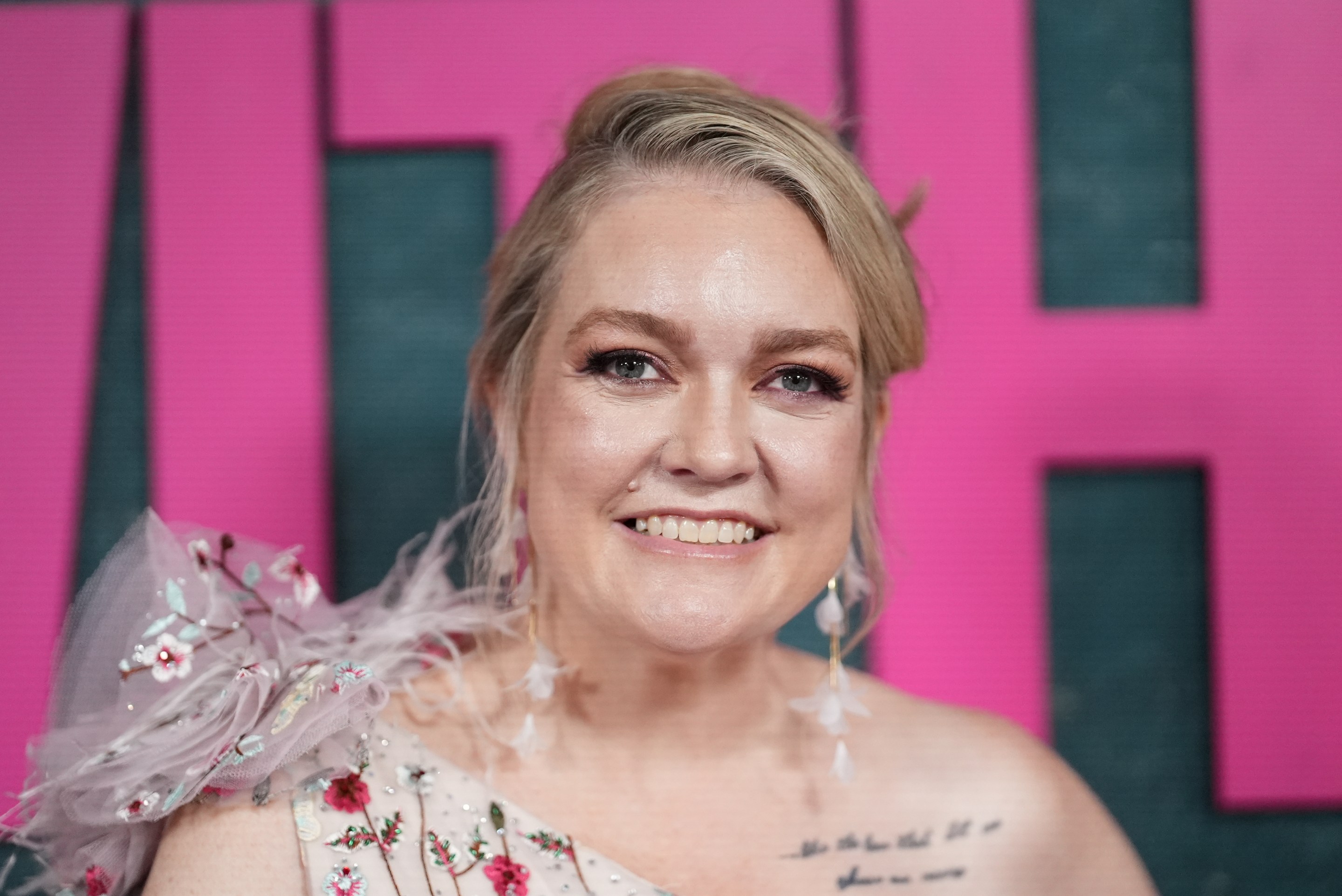 Colleen Hoover, wearing a one-shoulder dress, smiles at the camera.