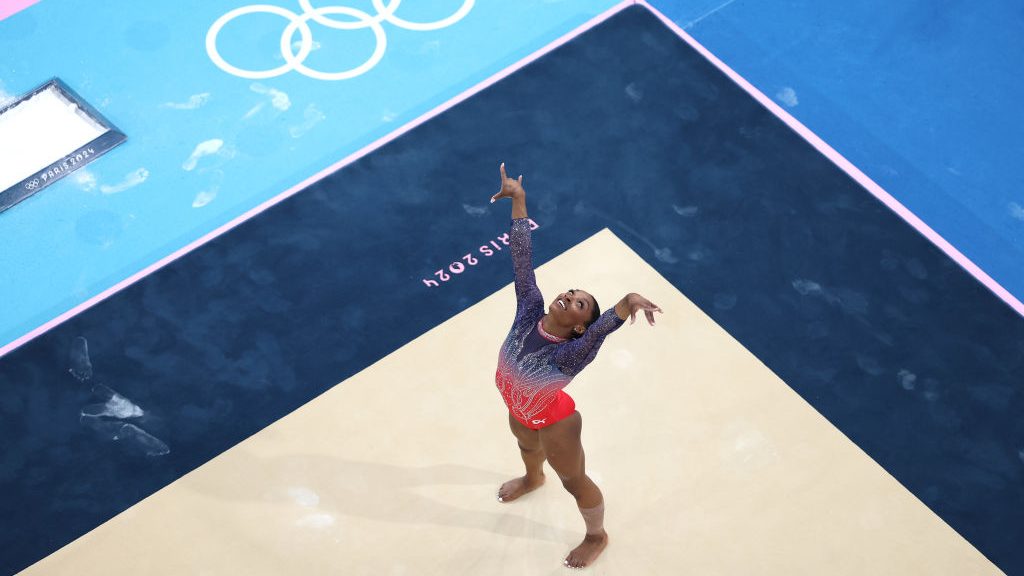 Simone Biles of Team United States competes in the Artistic Gymnastics Women's Floor Exercise Final on day ten of the Olympic Games Paris 2024 at Bercy Arena on August 05, 2024 in Paris, France. Her arms are up in the air, and she is smiling.