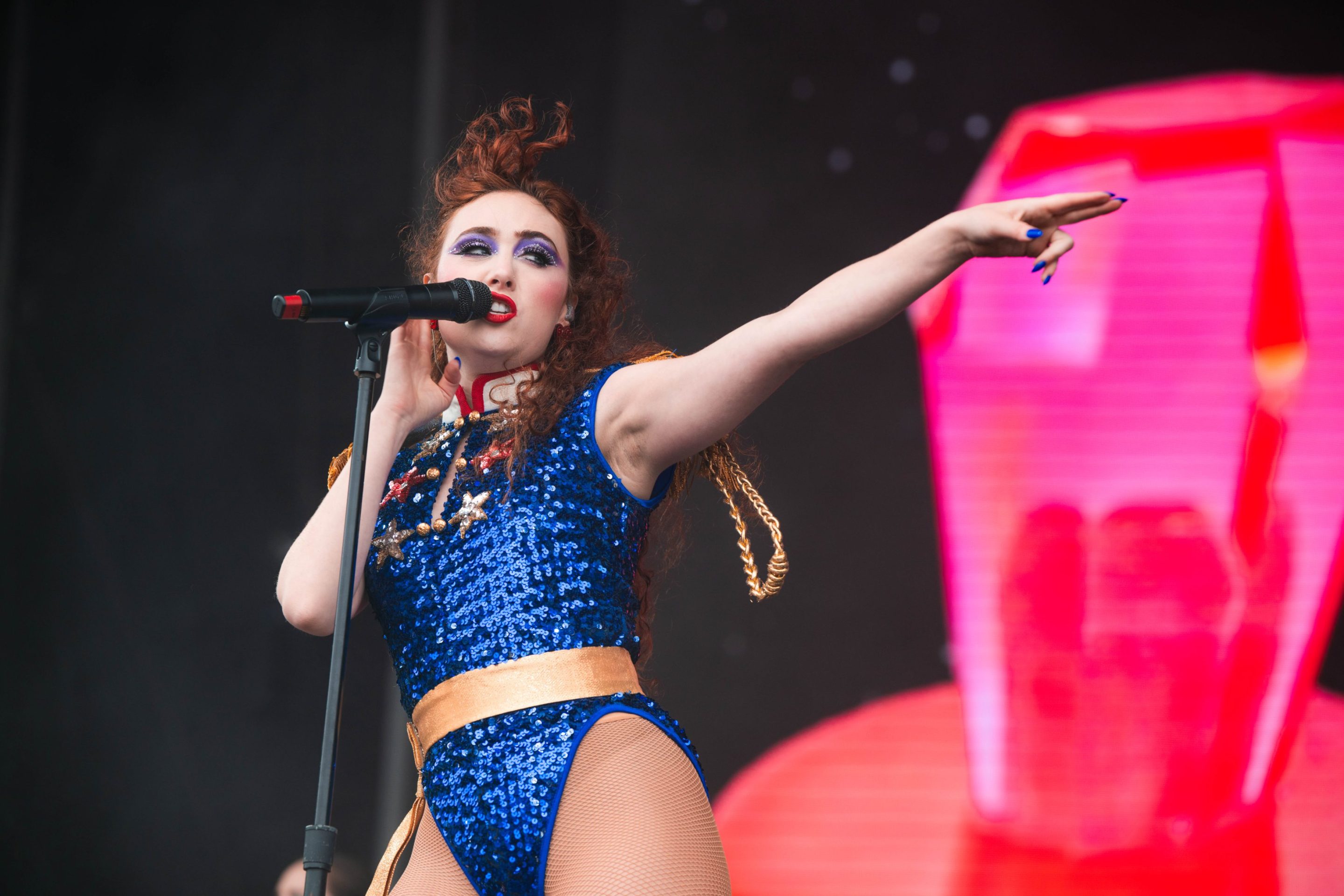 Chappell Roan on stage in a blue outfit, her hair blowing behind her, with one arm outstretched, pointing.