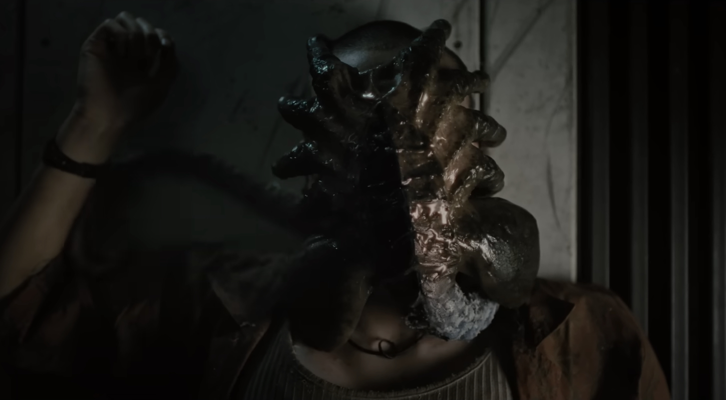 A gross alien facehugger, clamped onto a character's face in Alien: Romulus.