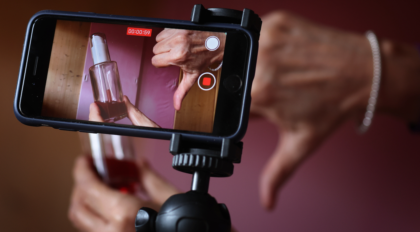 A woman sticks her thumb down next to a skincare product and records the scene with an iPhone (posed scene). Product tips on Instagram or Tiktok are often paid advertising. "Deinfluencers" actively advise against buying if they are not convinced of the quality.